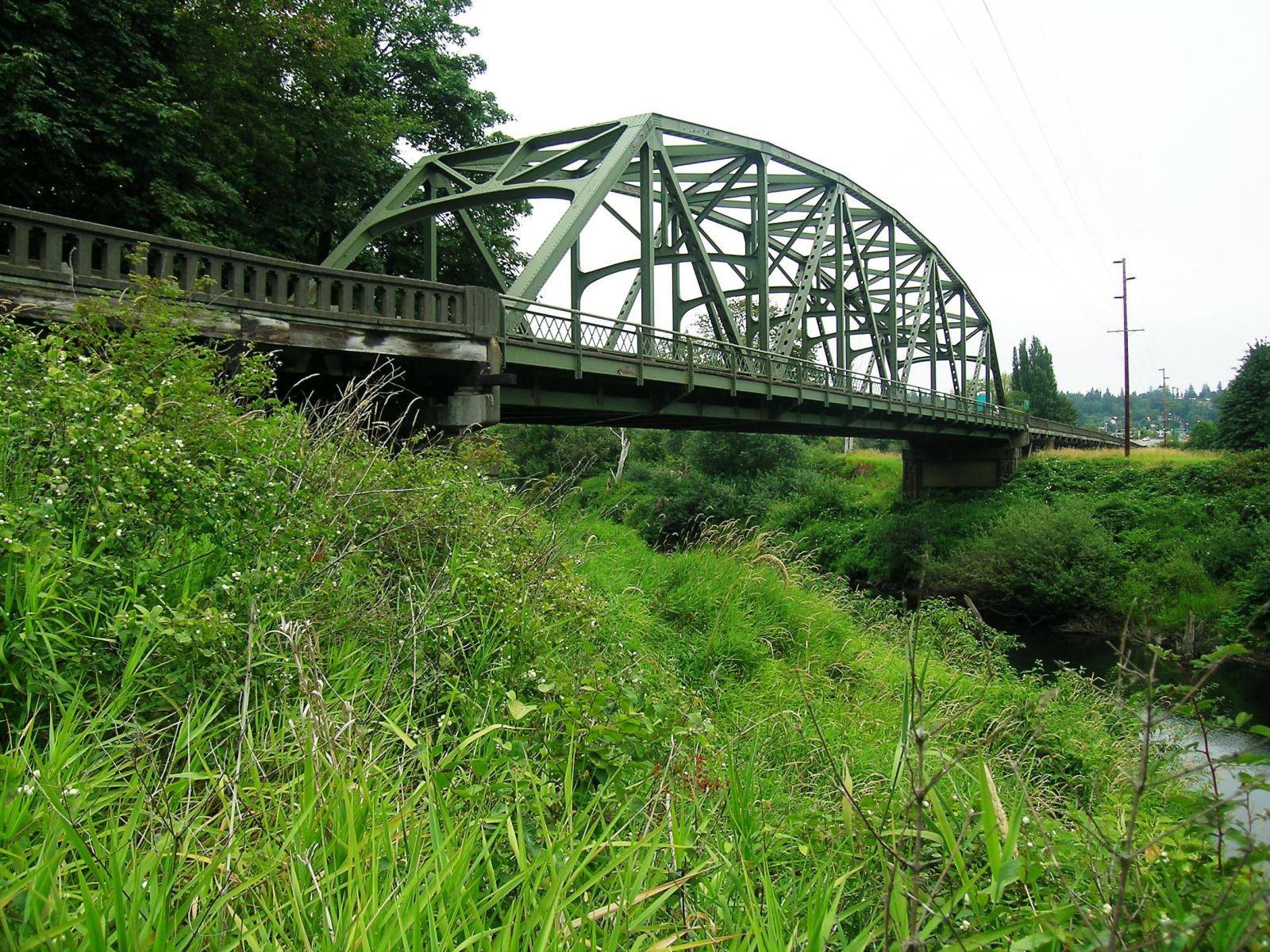 A photograph of a steel trestle bridge over a river with grassy banks.