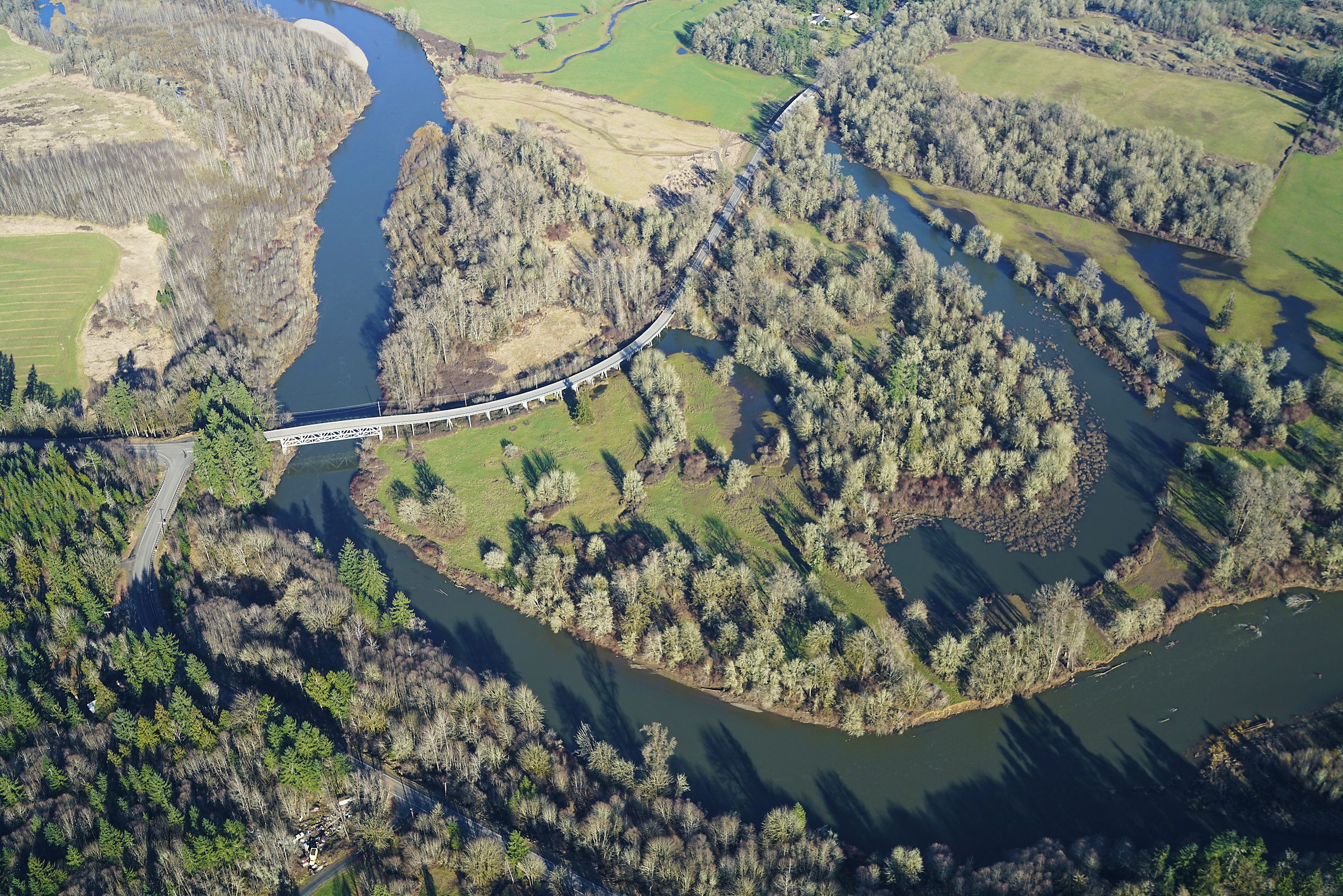 An aerial view of the Chehalis River showing an elevated roadway, trees, and wetlands.